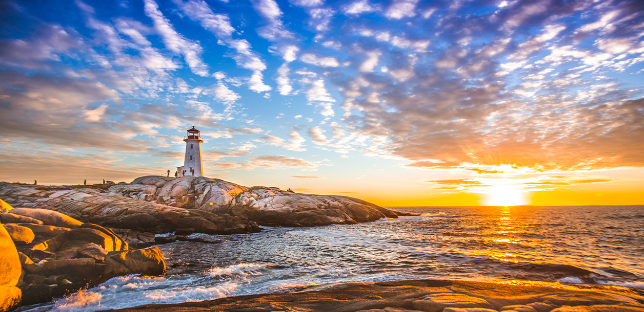 A lighthouse on a rocky cliff overlooks the ocean at sunset
